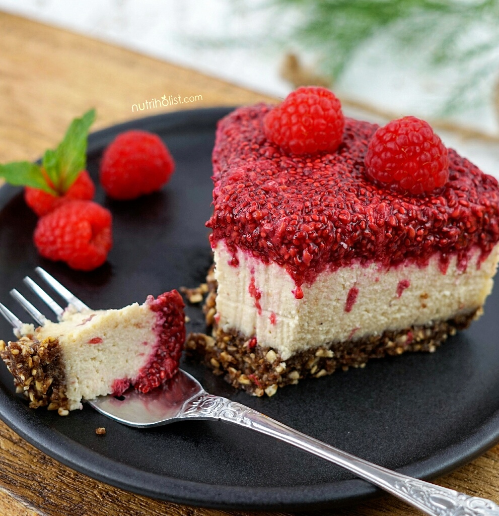 Raspberry Chia Cheesecake slice decorated with fresh raspberries on a black plate with a fork that holds a bite
