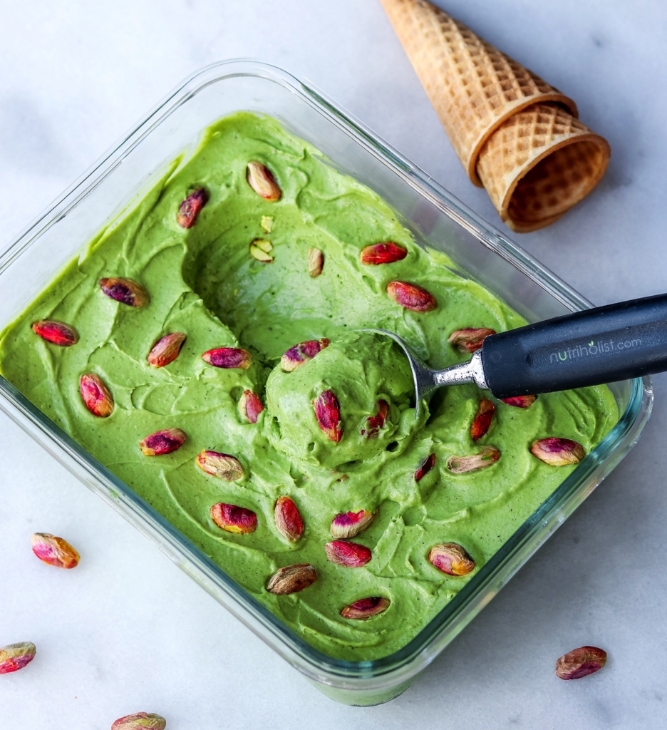 Using an ice cream scooper to grab a scoop of creamy Vegan Pistachio Ice Cream topped with pistachios
