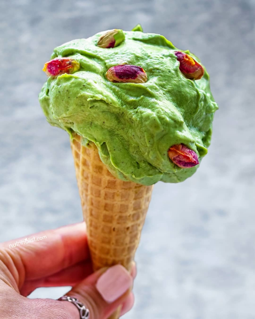 A scoop of Vegan Pistachio Ice Cream in a waffle cone topped with pistachios