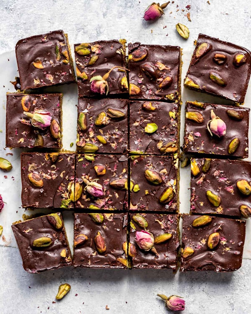 Dark Chocolate Pistachio Bars topped with pistachios and rose petals, cut into squares, top view.