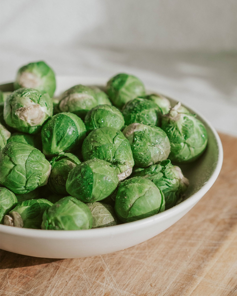Brussels Sprouts washed in a white bowl on a wooden cutting board
